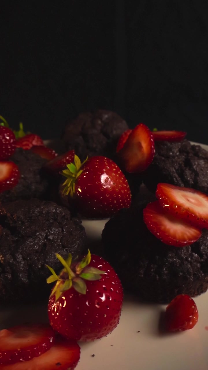 Primo piano di muffin al cioccolato fatti in casa elegantemente disposti su un piatto con fragole fresche intere e a fette, che evidenzia la ricca consistenza del dessert con un movimento fluido.