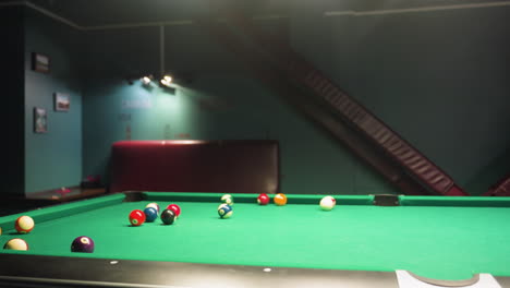 billiard balls scattered across green pool table after break shot in motion. tiled wall with country names visible in background. dynamic shot captures movement, energy