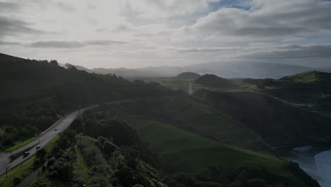 Toma-Aérea,-Punto-De-Drone-De-Automóviles-Conduciendo-Por-Una-Ruta-Escénica-Con-Nubes-Y-El-Telón-De-Fondo-Del-Amanecer-De-Sao-Miguel,-Azores,-Portugal