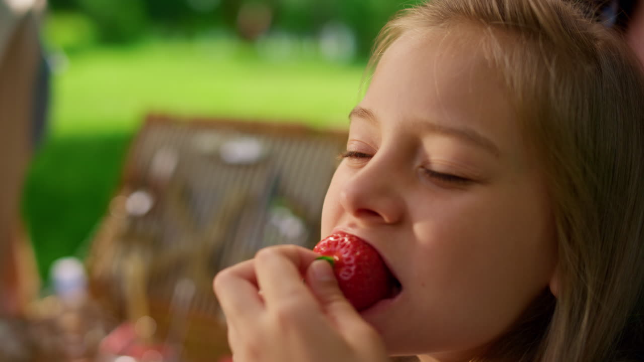 Pretty girl eating strawberry on summer picnic close up. Blond child taste berry