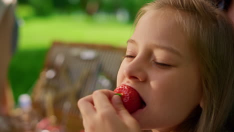 pretty girl eating strawberry on summer picnic close up. blond child taste berry