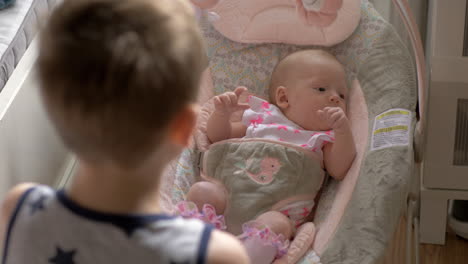 brother rocking baby sister in chair at home