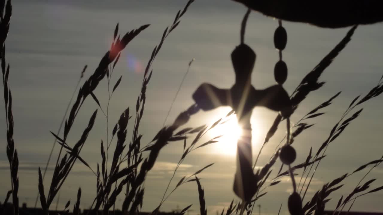 Fingers holding rosary beads against sunset in rural scene
