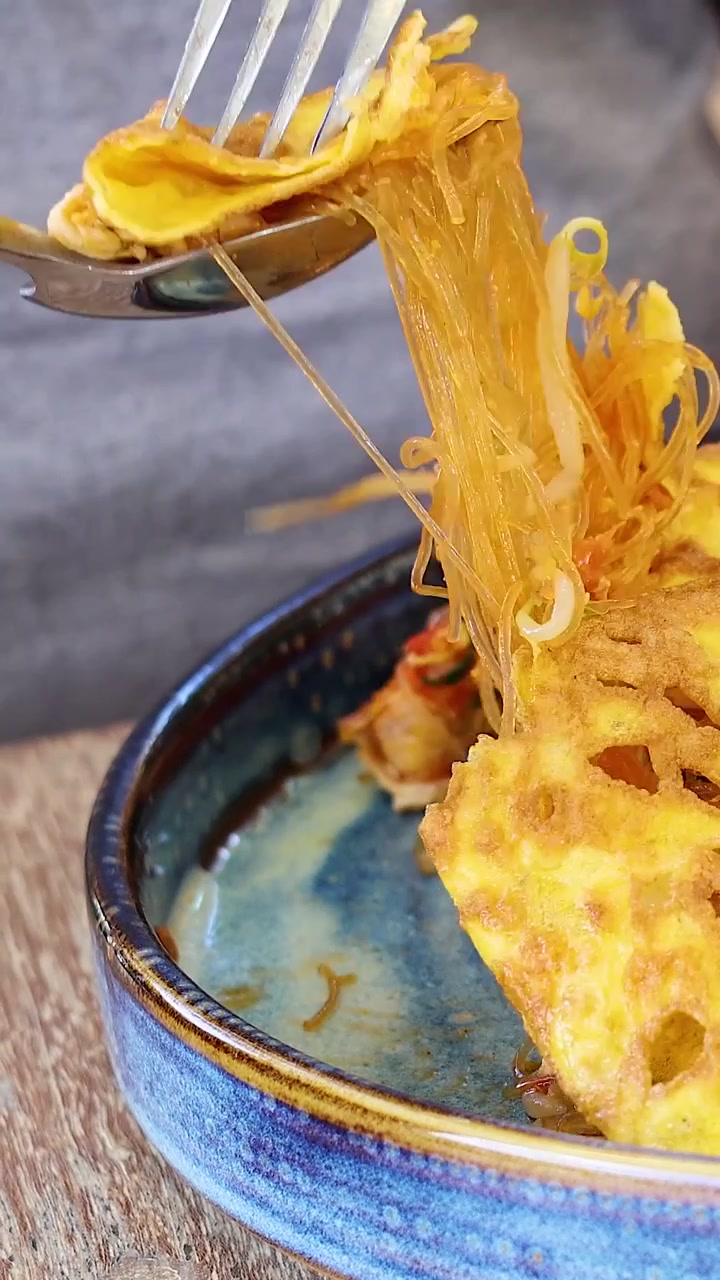 Persona che mangia pad thai da un piatto di ceramica