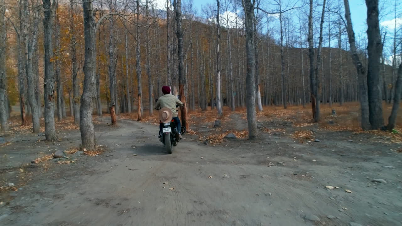 Solo traveler biker riding in the woods on a sports bike during autumn season in a low height establishing aerial shot.