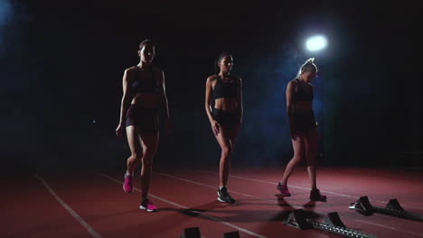 three girls in black clothes are in the starting pads to start the race in the competition in the light of the lights and run towards the finish