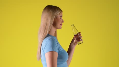 side view of blonde woman drinking water from glass bottle, studio portrait