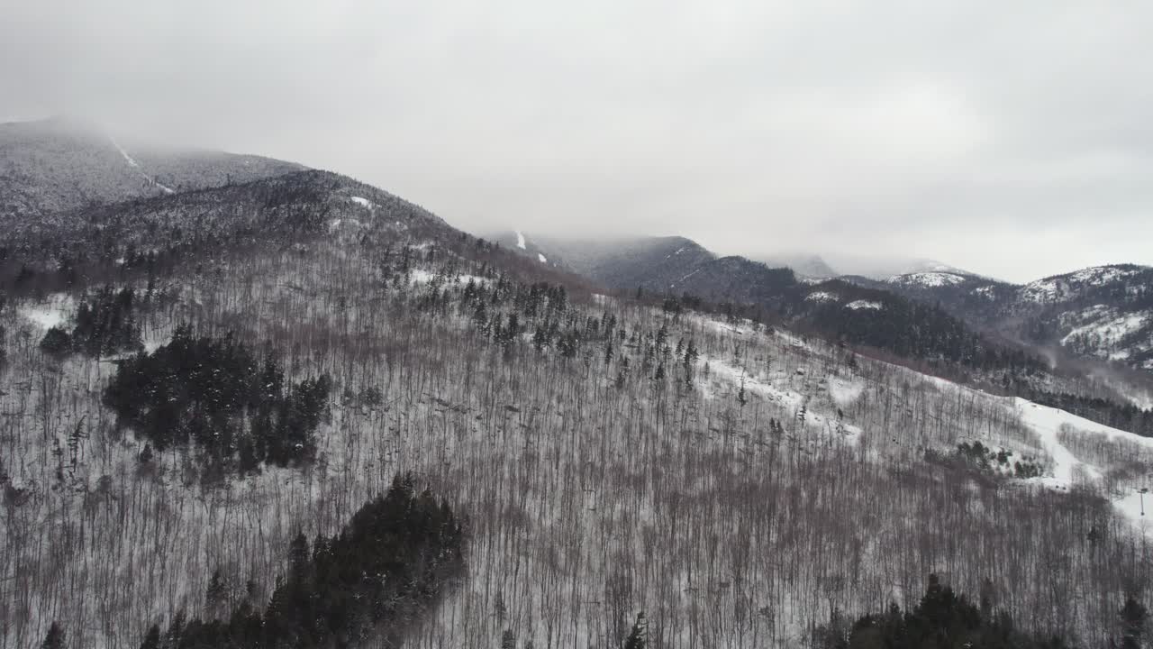 A slow rising drone shot with a dramatic low cloud ceiling shrouding the top of Whiteface Mountain in the Adirondacks, upstate NY during midwinter.