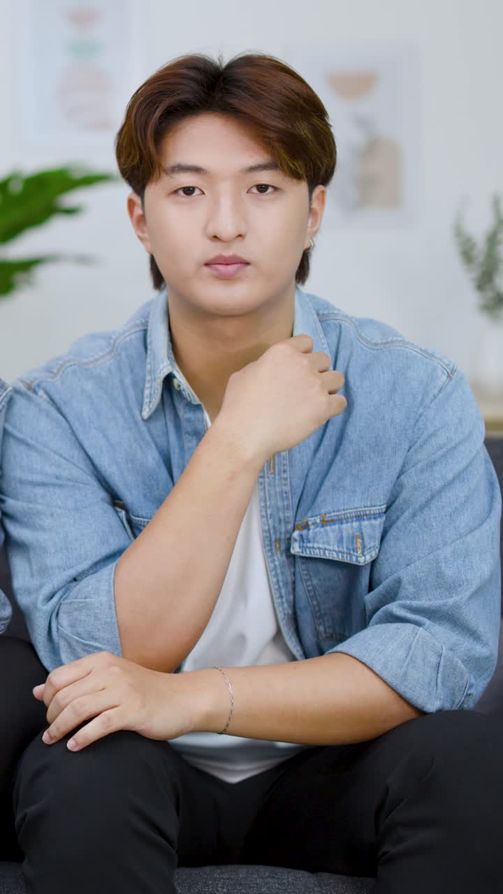 ชายหนุ่มชาวเอเชียนั่งอยู่บนโซฟา ตั้งใจดูโทรทัศน์พร้อมกับการแสดงออกทางสีหน้าที่เปลี่ยนไป