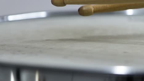 close-up-drumsticks-tips-hitting-steel-snare-drum-head-against-white-background