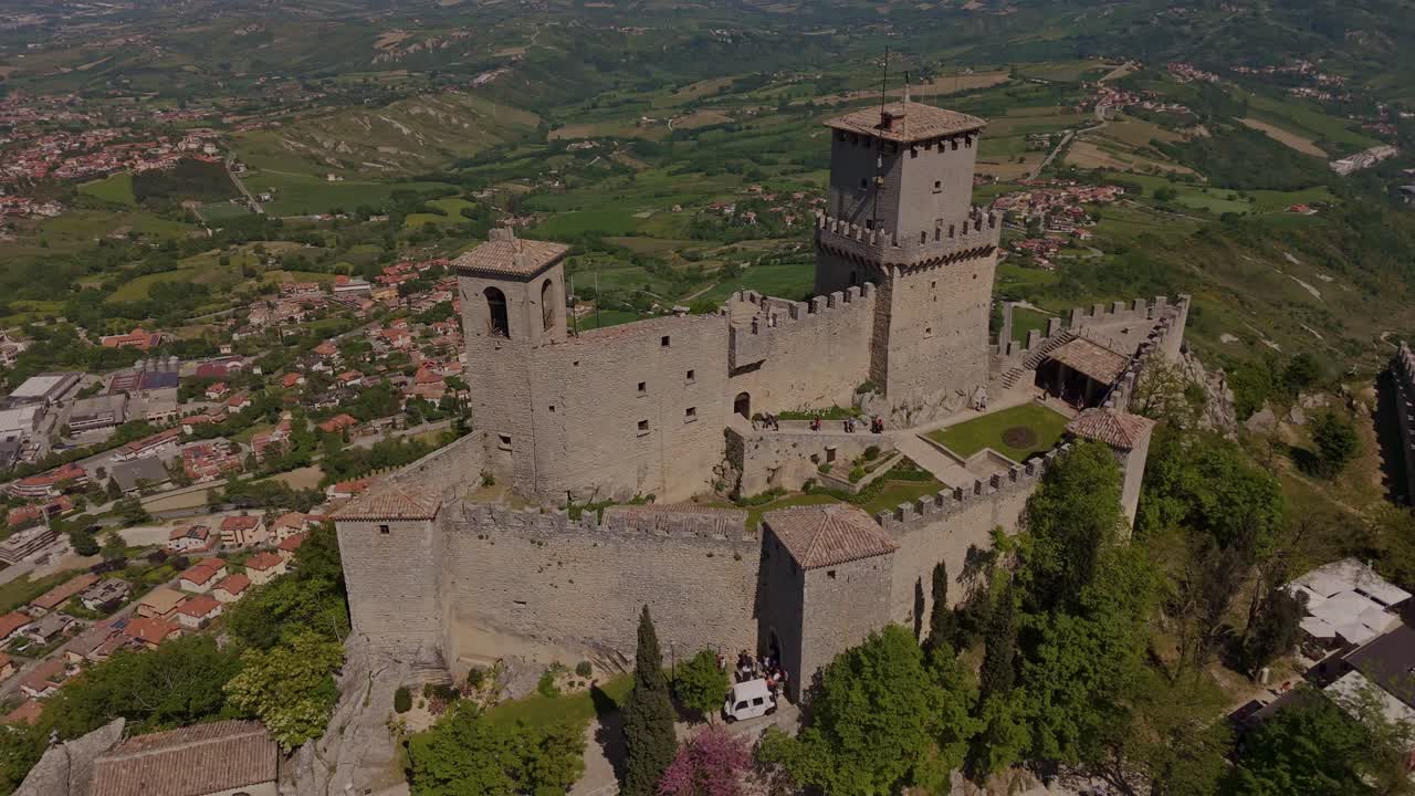 Dramatic drone orbit of Guaita Tower, also known as La Rocca or Prima Torre, San Marino’s oldest fortress atop Monte Titano. Medieval stone walls and towers dominate the lush surrounding hills.