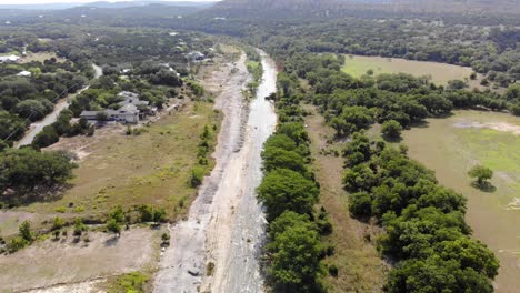 Flying-in-direction-of-the-sun-over-the-river-towards-large-homes---recreational-areas---Aerial-footage-of-the-Blanco-river-in-Wimberly,-TX