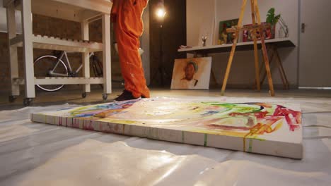 Low-section-of-african-american-male-artist-pouring-paint-on-canvas-at-art-studio