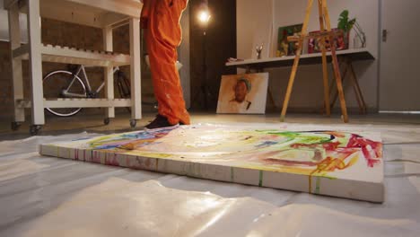 sección baja de artista masculino afroamericano vertiendo pintura en el lienzo en el estudio de arte