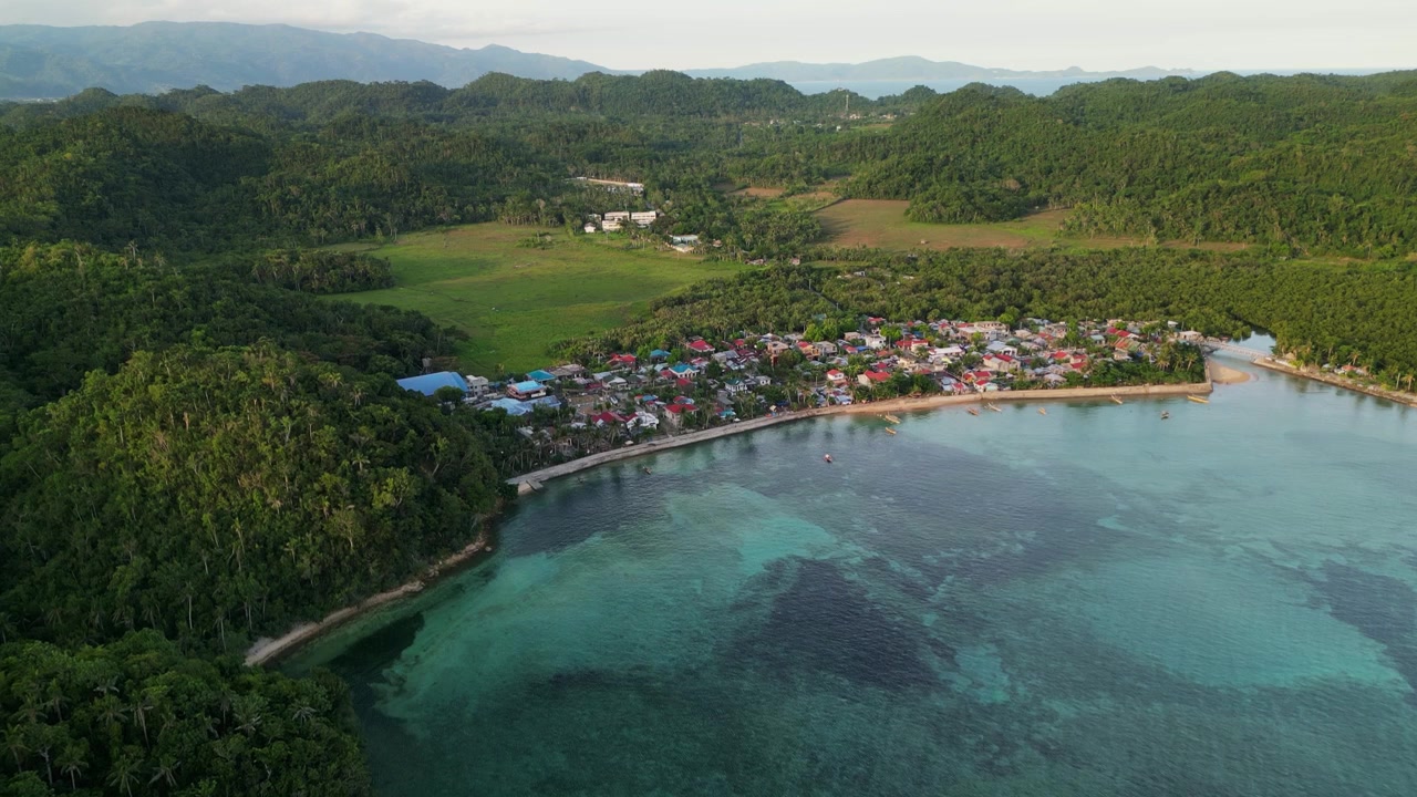 Vista aerea panoramica di Magnesia Del Norte a Virac, Catanduanes, con un villaggio costiero, acqua limpida della baia e lussureggianti colline tropicali.