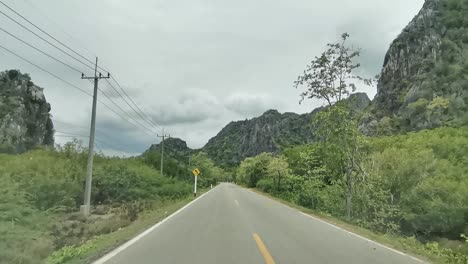 driving between limestone rocks and mountainous terrain with green trees surrounding the road, thailand