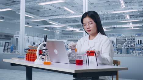side view of asian woman scientist making experiment with test tube, typing on a laptop, celebrating success in laboratory with microscope. working in the lab analyzing finding sample test tube