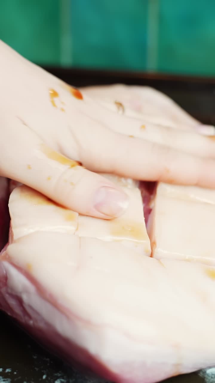 Macro vertical de uma mão esfregando marinada picante de soja na pele de barriga de porco marcada em uma bandeja, preparando torresmo crocante para assar