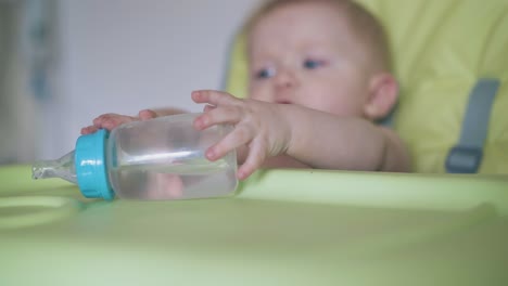 Besorgtes-Baby-Mit-Flasche-Sitzt-Im-Hochstuhl-An-Der-Weißen-Wand