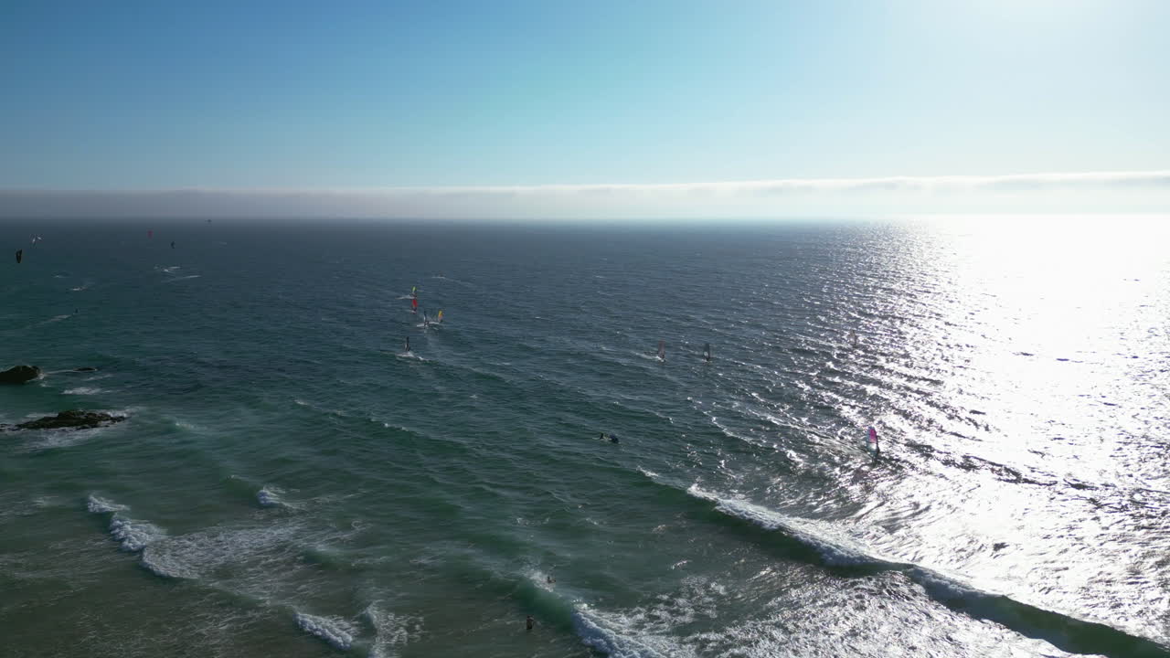 Panoramic drone shot of kite surfers, surfing in waves of sunny Guincho, Portugal