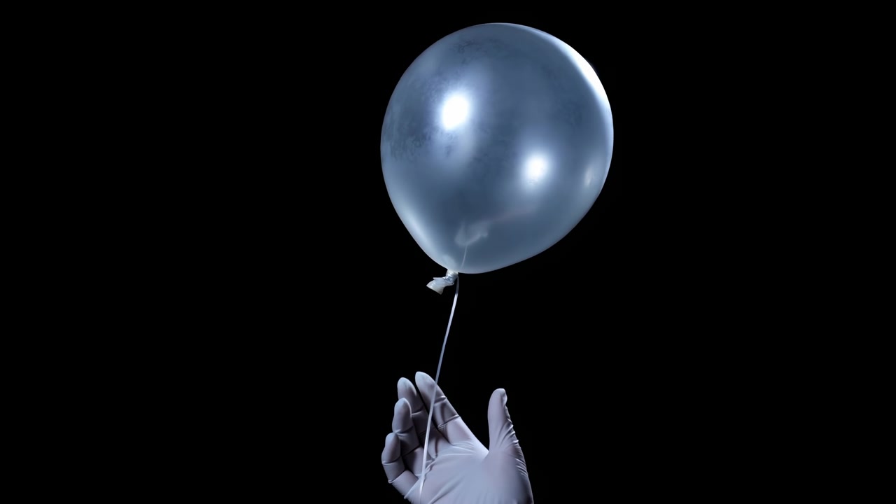 Vista cercana muestra una mano enguantada que se aleja mientras un globo azul reflectante se eleva a través del espacio negro, con una cuerda delicada, reflejos suaves en la superficie y una composición simple y centrada.