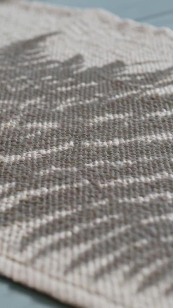 Video verticale: Luce solare che si sposta, proiettando ombre di felci su un tessuto beige su un tavolo blu, mostrando la trama.