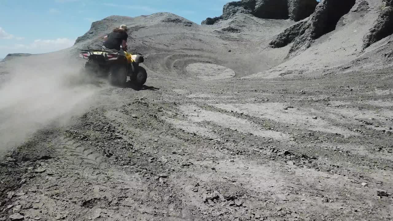 Following Man Driving ATV Quad and Making Dust in Utah Desert Under Black Sandstone Cliff, Factory Butte Region USA, Aerial View