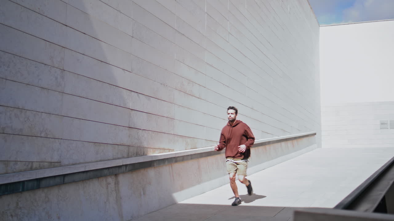 Runner jogging modern architecture in sunny morning. Motivated man doing cardio