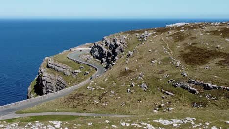 car driving along scenic green mountain country road overlooking gorgeous blue irish sea aerial push in tilt down