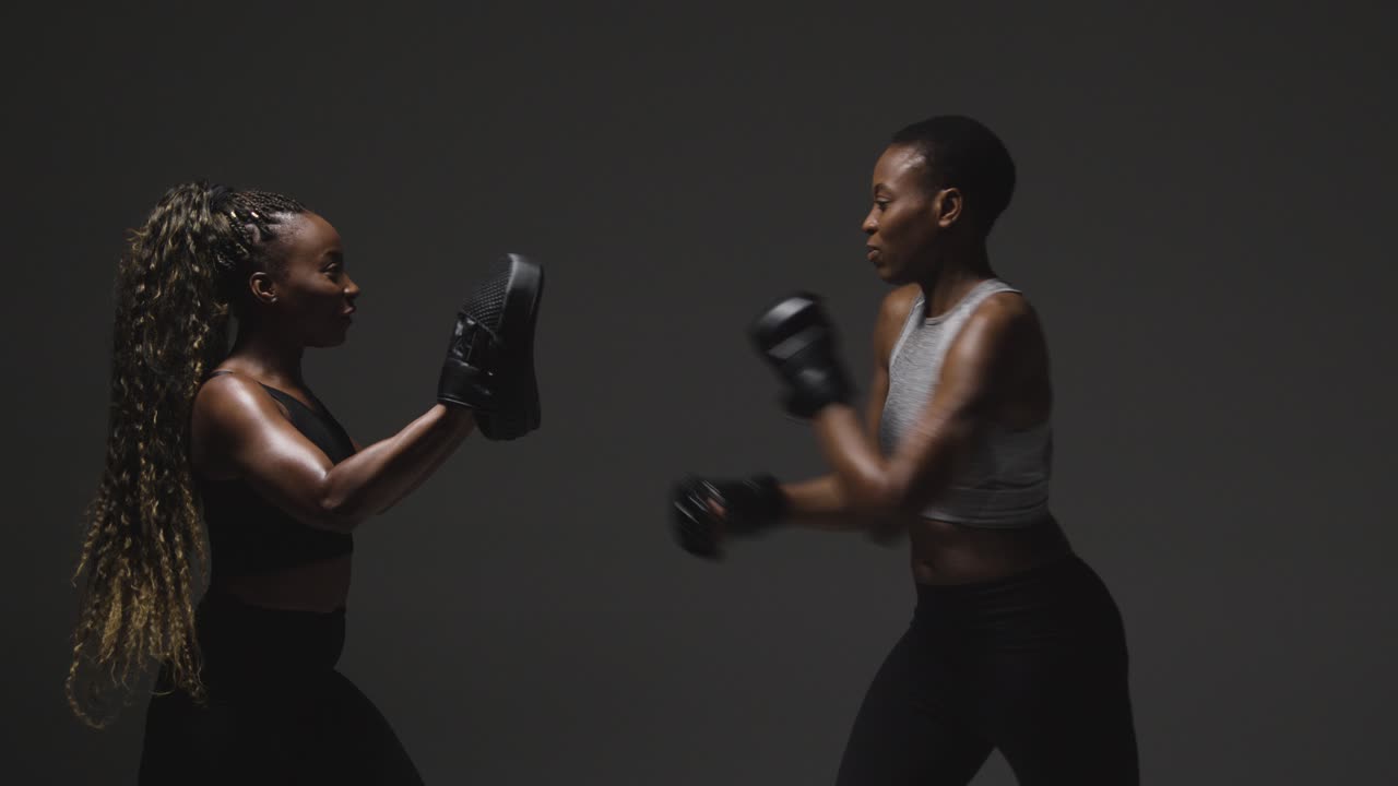 Studio Shot Of Woman Wearing Boxing Gloves Sparring With Trainer