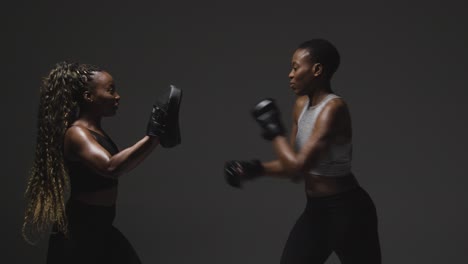 studio shot of woman wearing boxing gloves sparring with trainer