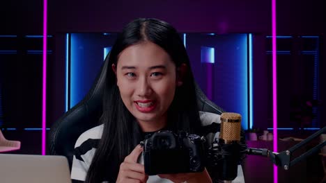 close up of a smiling asian woman with computer reviewing camera in room lit by neon lights in retro
