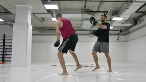 Coach-and-kick-boxers-practice-kicks-in-the-jump-with-rotation-on-the-paws-in-slow-motion.