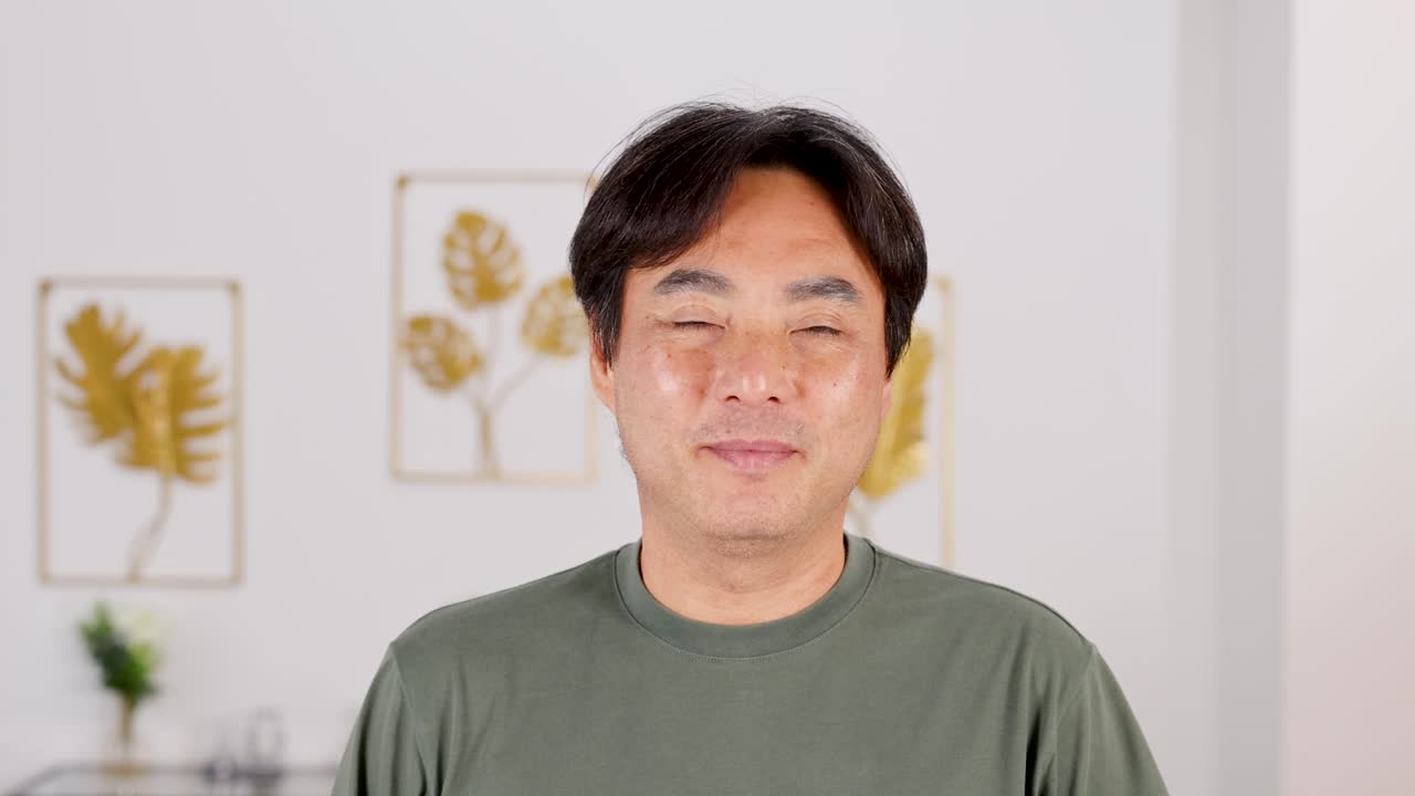 A man in a green shirt smiles gently in a well-lit room with decorative wall art