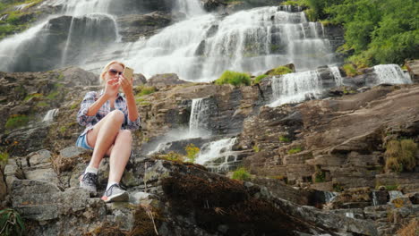 a traveler uses a smartphone against the background of a waterfall tvindefossen in norway 4k video