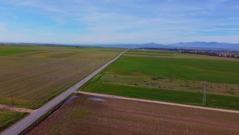 aerial view of straight empty road surrounded by green meadows and crop fields