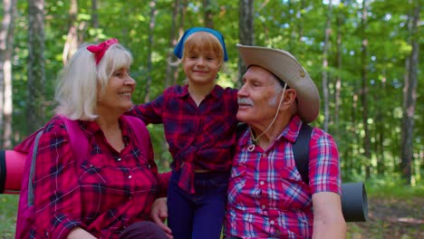 Grandmother-grandfather-and-child-kid-girl-family-hikers-tourists-sitting-in-wood,-hugging,-kissing