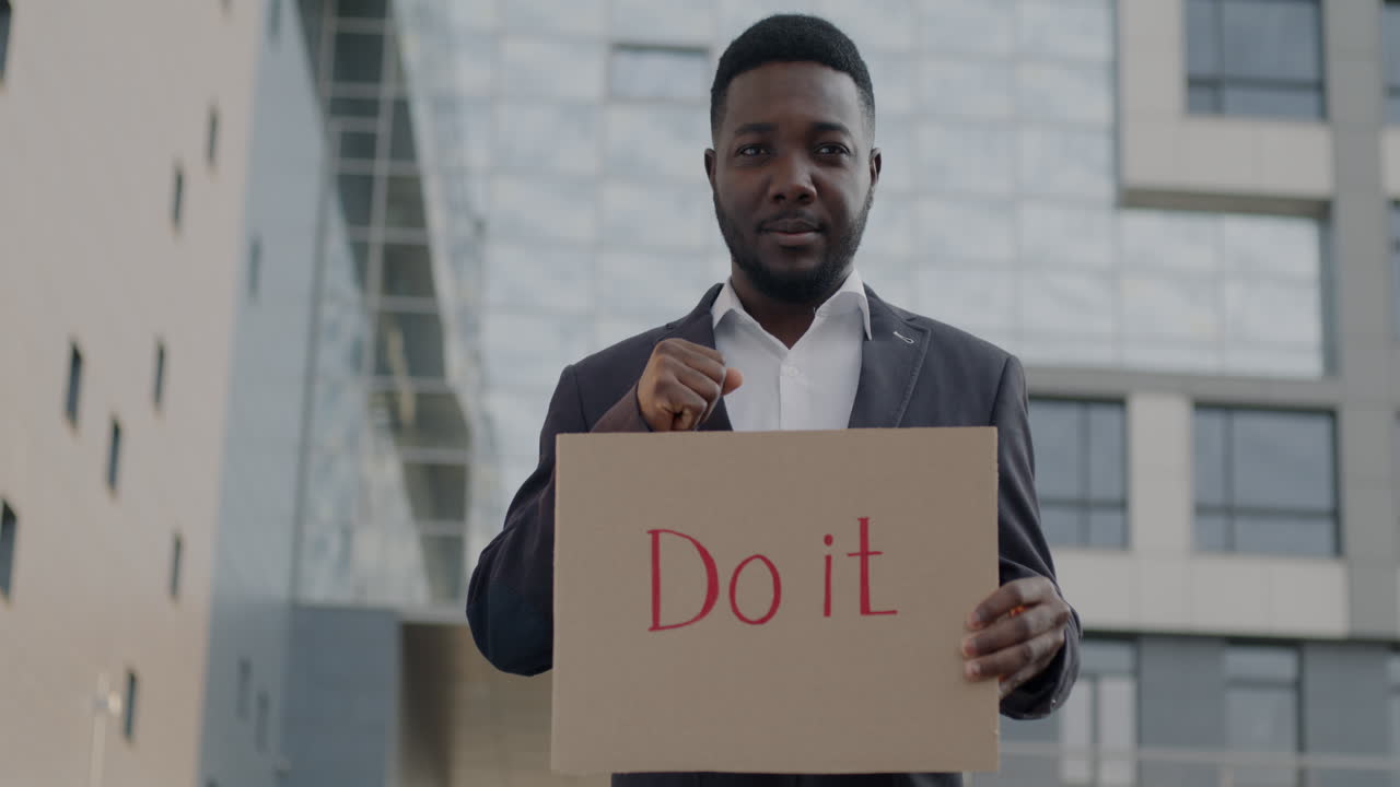Man holding a sign saying "Do It" in front of a building