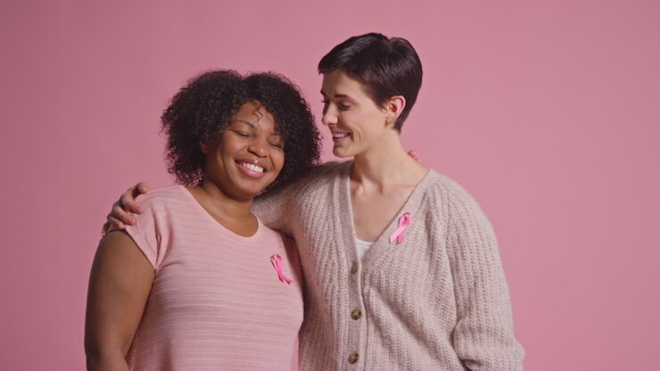 Studio Portrait Of Two Women Proud Of Pink Breast Cancer Awareness Ribbons Hugging Against Pink Background 1