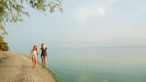 Mom-And-Daughter-Walk-Along-The-Picturesque-Beach-Where-The-Blue-Sky-Merges-With-The-Water