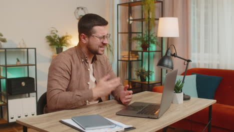 smiling young man freelancer having video call via laptop sitting at home office desk in living room