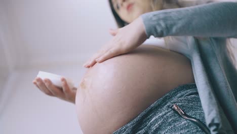 una joven mamá embarazada aplica loción en un primer plano del vientre grande
