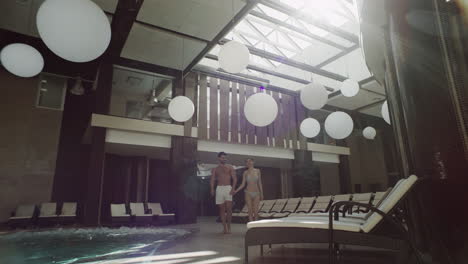 Romantic-couple-walking-indoor-pool.-Happy-couple-holding-hands-poolside