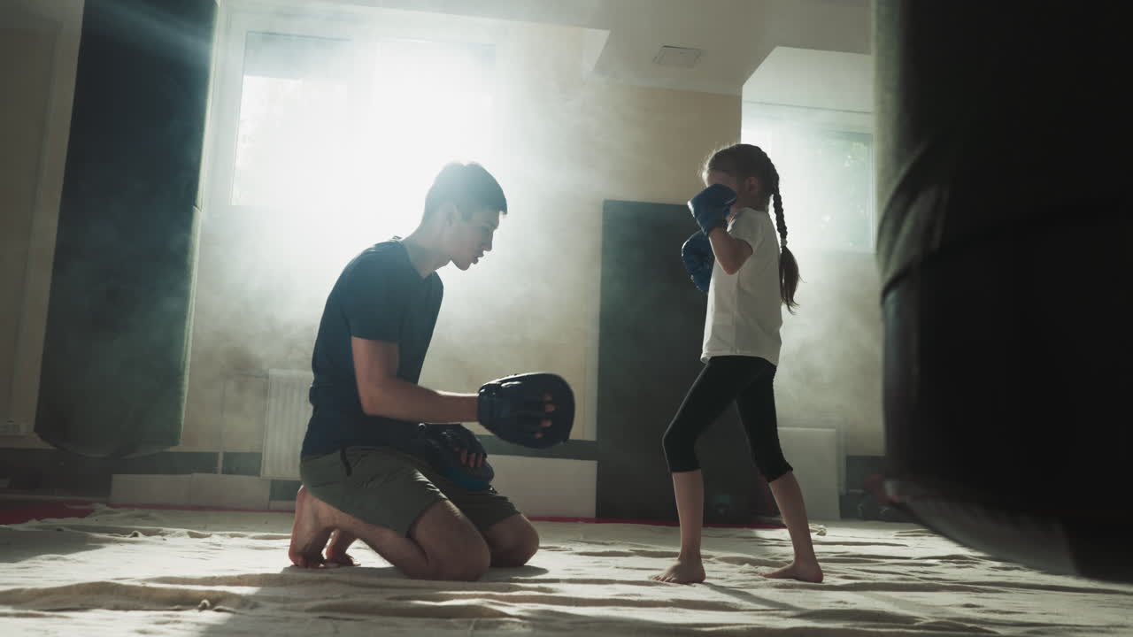 Child kicks pad under trainer control in gym. Combat trainer works with little girl upon leg attack in sports club slow motion. Martial arts school