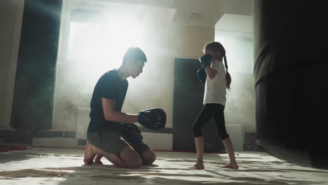 child kicks pad under trainer control in gym. combat trainer works with little girl upon leg attack in sports club slow motion. martial arts school