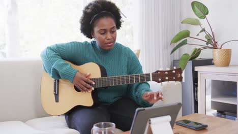 Feliz-Mujer-Afroamericana-Practicando-Tocar-La-Guitarra-Usando-Tableta-En-Casa,-Cámara-Lenta