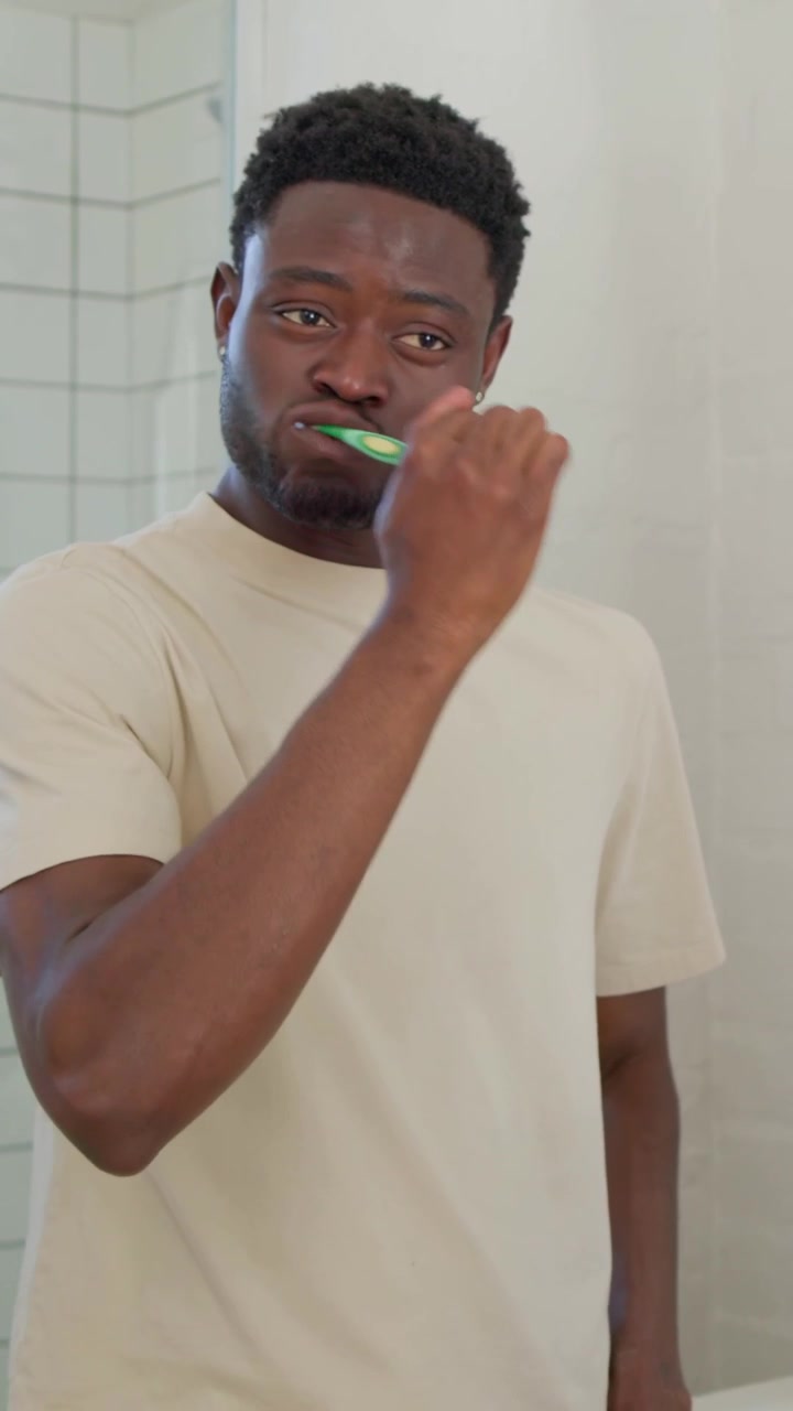 Vertical video: Picking up toothbrush and paste, man brushing teeth at home vanity for oral care