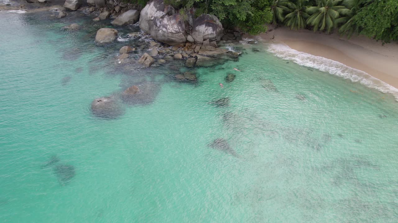 Filmato aereo della spiaggia di Sunset sull'isola di Mahe, coppia di turisti che fanno snorkeling vicino agli scogli, acqua cristallina, Mahe Seychelles 30fps 003