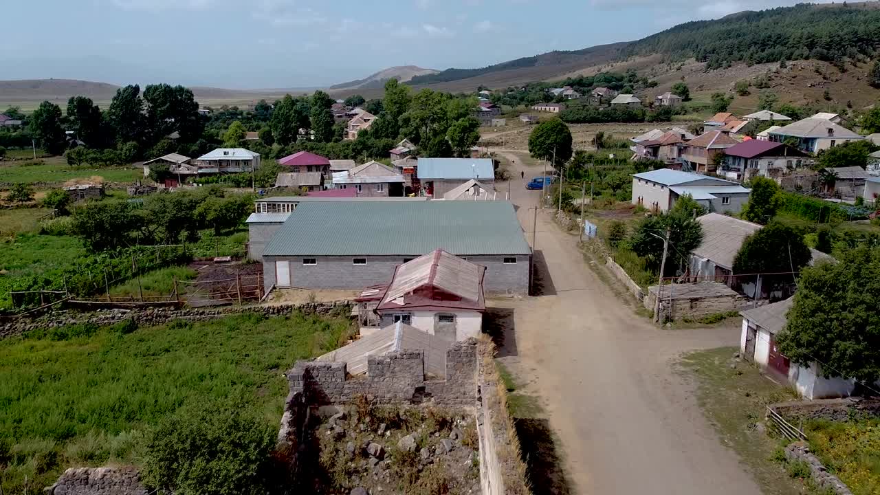 This clip showcases a serene village landscape with houses nestled among hills. Residents engage in daily activities on a sunny day, highlighting rural life and community