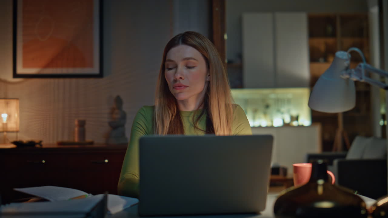 Tired girl student studying laptop late evening in dark apartment close up.